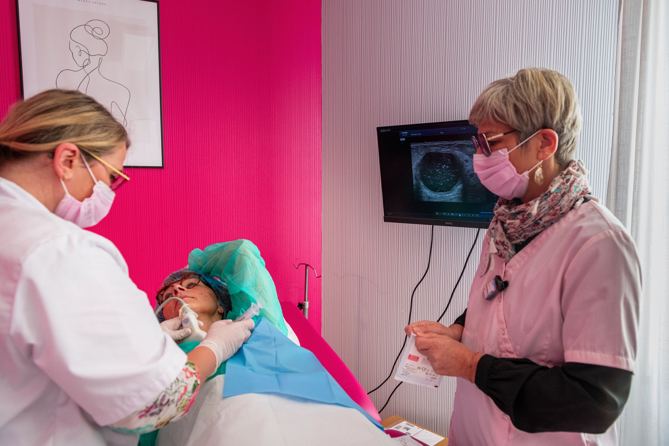 Radiologue pratiquant une procédure de microbiopsie mammaire échoguidée, assistée par une manipulatrice radio.